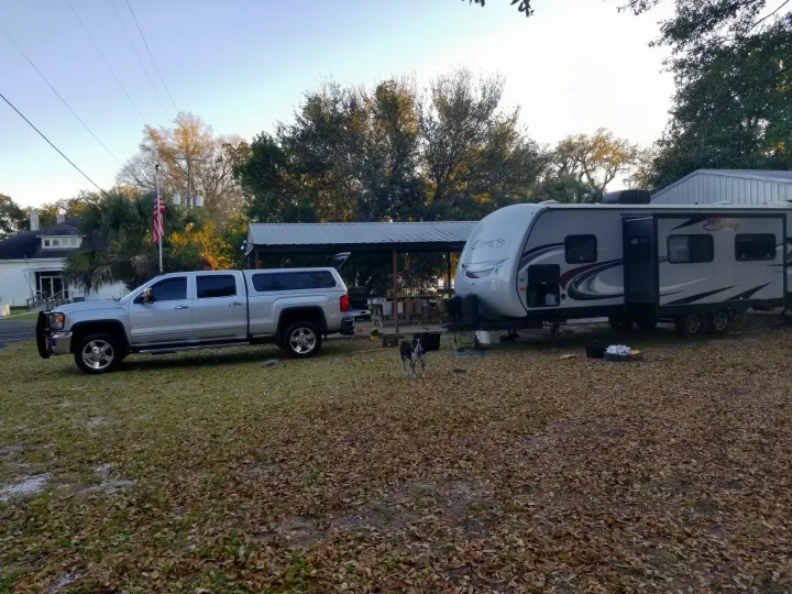This RV rental features a silver pickup truck & spacious travel trailer parked in a leafy yard. A dog observes the scene.. KZ Spree 301RIK 2015