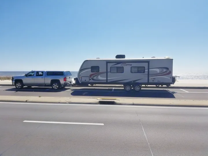 Silver pickup truck towing a grey RV rental by the ocean on a sunny day. Ready for adventure!. KZ Spree 301RIK 2015
