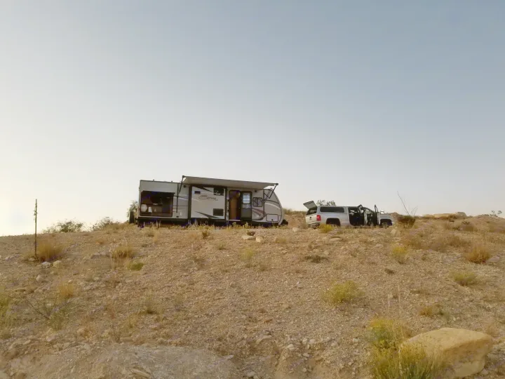 RV rental and truck parked on a dry, rocky hillside with awning out, set up for remote camping.. KZ Spree 301RIK 2015