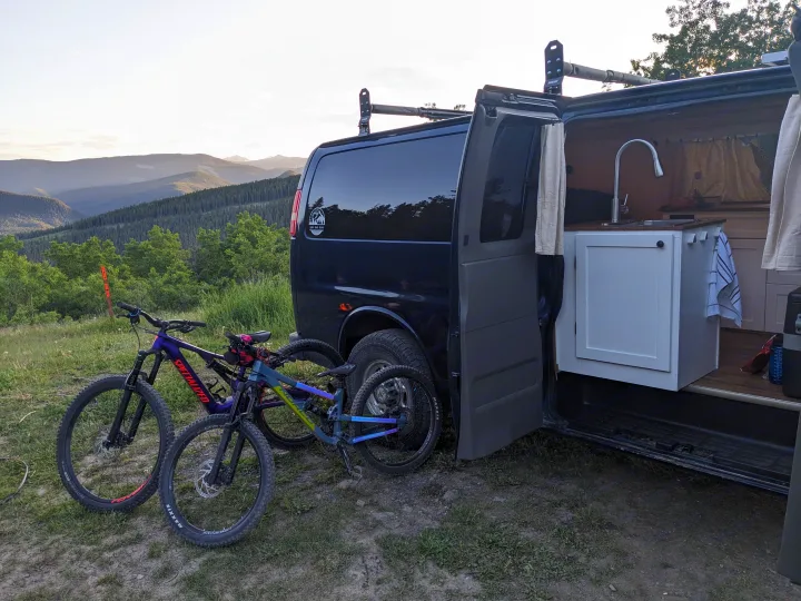 RV rental camper van with mountain bikes, kitchen setup, and scenic mountain views. Perfect for adventure!. Chevrolet Express 2003