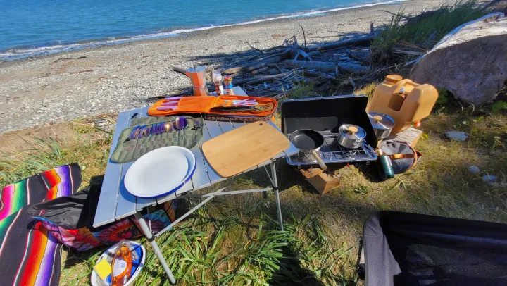 RV rental travelers enjoy a sunny beachfront cooking setup with portable stove, table, and iridescent cutlery.. MITSUBISHI Delica 1997