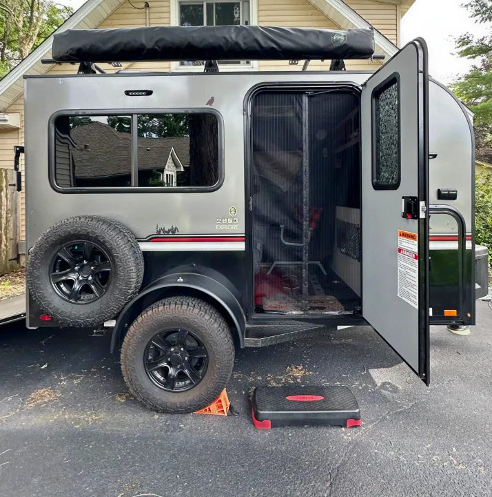 Compact off-road travel trailer, ideal for an RV rental adventure, parked in a driveway. The door is open, showing its interior.. Intech Explore 2023