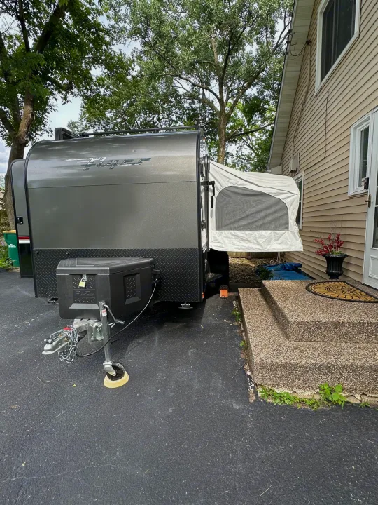 Grey Flyer travel trailer, a compact pop-up camper for your next RV rental, parked beside a house. Ready for adventure.. Intech Explore 2023