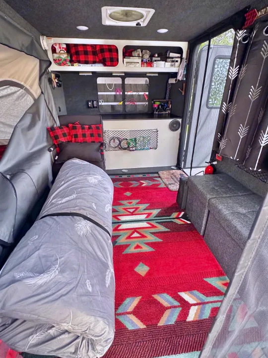 An inviting RV rental interior featuring a rolled bed, smart storage solutions, and a vibrant Southwestern rug.. Intech Explore 2023