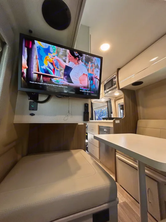 RV rental's functional interior: mounted TV, compact kitchen, dining area, & bed for comfortable travel.. Thor Tellaro 2024