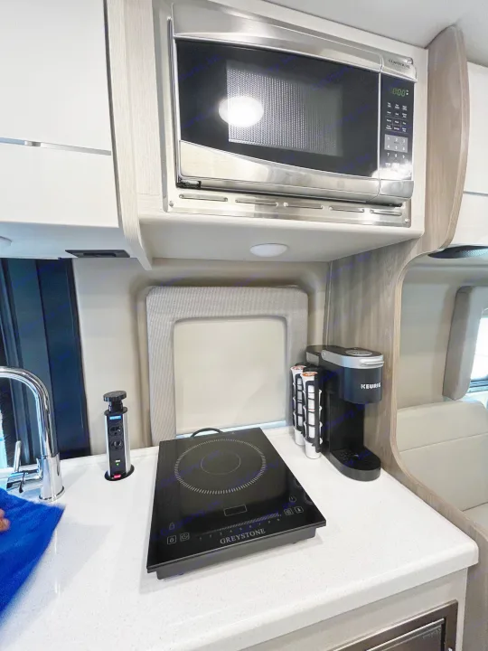 Well-equipped RV rental kitchen: microwave, induction cooktop, Keurig coffee maker, and pop-up counter outlets.. Thor Tellaro 2024