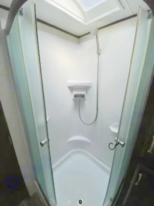 Interior of a white, compact corner shower with glass doors, handheld showerhead, & shelves, common in an RV rental.. Jayco Jay Flight 2018