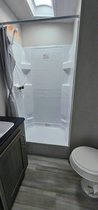 Compact RV rental bathroom: corner shower, skylight, sink vanity, and toilet with modern finishes.. Keystone Fuzion 2024