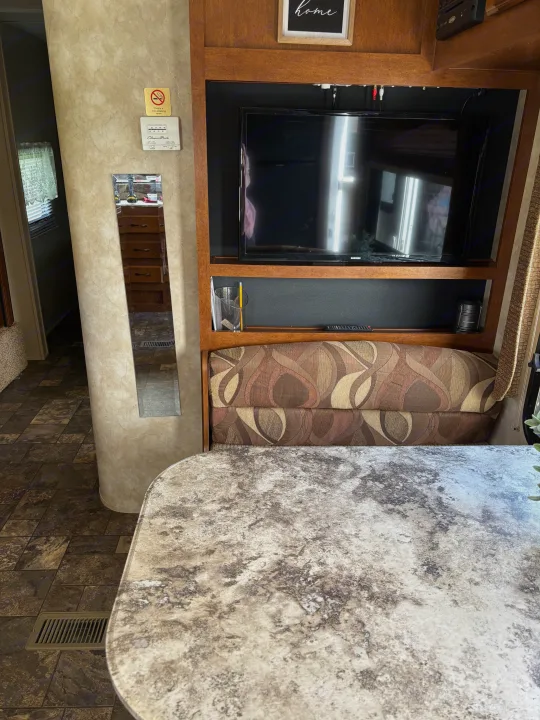 Inside this RV rental: a dining area featuring a patterned booth, table, and entertainment center with a TV.. Coachmen Catalina Deluxe Edition 2013