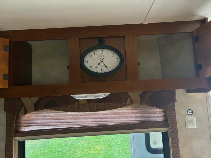 RV rental interior: Overhead cabinets with a clock, window blinds, and light switches are visible.. Coachmen Catalina Deluxe Edition 2013