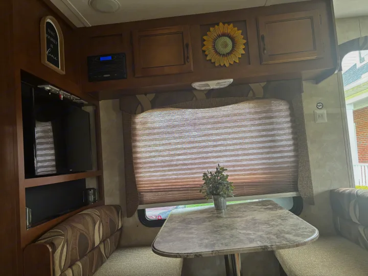 Inviting RV rental interior: a cozy dinette, TV, stereo, overhead storage, and a 'make yourself at home' sign.. Coachmen Catalina Deluxe Edition 2013
