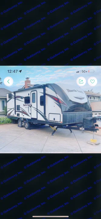 White & black North Trail travel trailer for RV rental, securely parked on a patterned concrete driveway.. Heartland RVs North Trail 2019