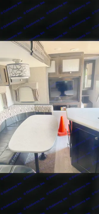 RV rental interior featuring a dinette, entertainment center with TV, and kitchen area. Orange safety cones are visible.. Heartland RVs North Trail 2019
