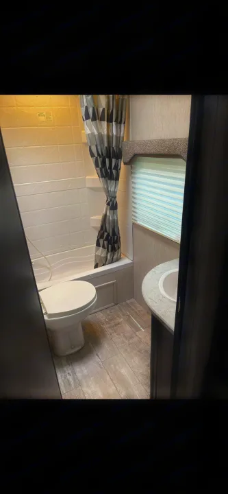 This RV rental bathroom features a white toilet, shower/tub, patterned curtain, and sink vanity. Functional layout.. Heartland RVs North Trail 2019