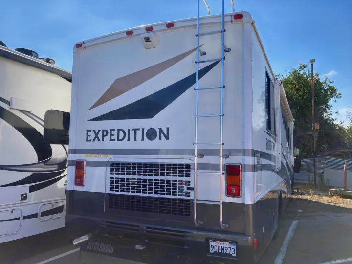 Rear view of a Fleetwood Expedition RV rental, a white motorhome with a ladder, parked outdoors.. Fleetwood Expedition 2003