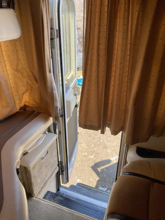 RV rental interior: open door with steps to outside, plush seating, and patterned curtains, ready for travel.. Fleetwood Expedition 2003