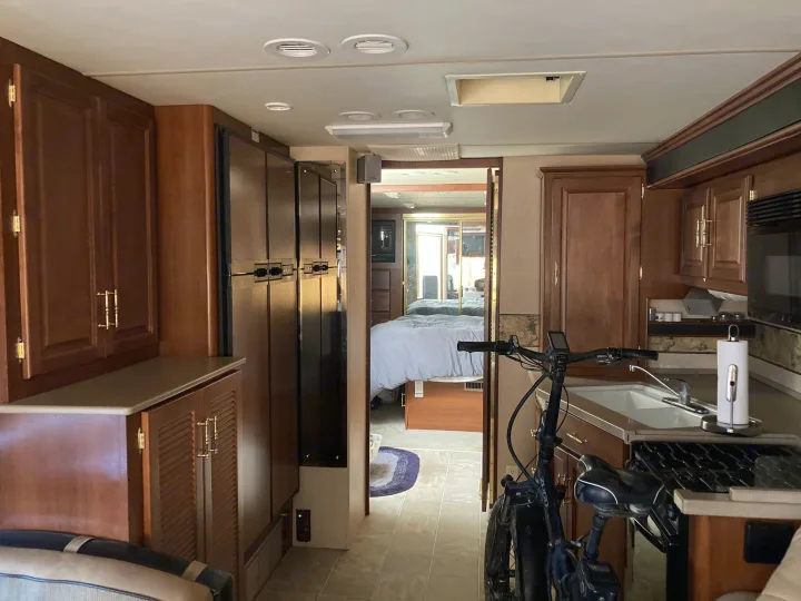 RV rental interior featuring a full kitchen, bedroom, and hallway. A folding bike sits by the counter.. Fleetwood Expedition 2003