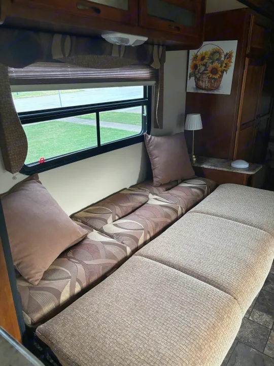 Comfortable RV rental interior with patterned and textured cushions, a sunny window, and overhead storage.. Coachmen Catalina Deluxe Edition 2013