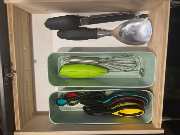 RV rental kitchen drawer: Organized cooking tools, including tongs, whisks, and colorful measuring cups/spoons.. Keystone RV Springdale 2022