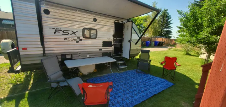 Relaxing outdoor setup with an RV rental. Awning extended, chairs, and mat ready for comfort in a sunny yard.. Forest River Salem FSX 2019