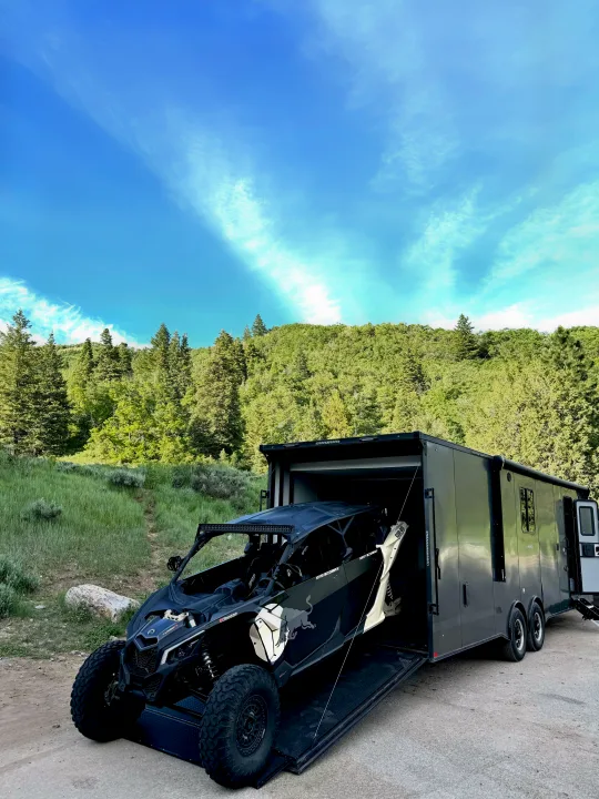 Toy hauler RV rental unloading a side-by-side for an outdoor adventure in a scenic mountain setting under a blue sky.. Stealth Nomad 28FK 2022