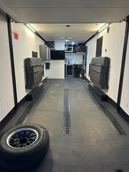 Spacious RV rental interior featuring diamond plate floor, fold-up benches, kitchenette, and tie-down tracks.. Stealth Nomad 28FK 2022