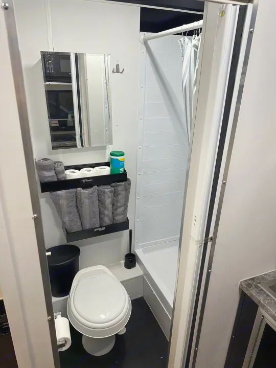 Compact RV rental bathroom with a functional shower, toilet, mirror, and organized storage for towels and supplies.. Stealth Nomad 28FK 2022
