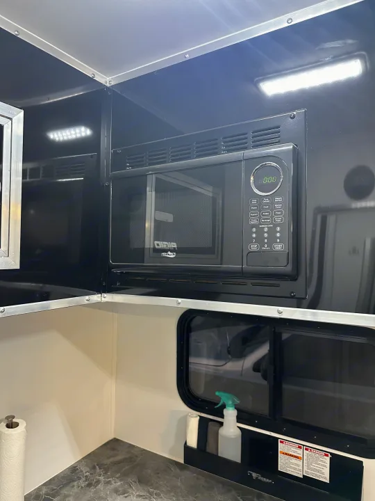 Modern RV rental kitchen interior featuring a mounted High Pointe microwave, spacious counter, and window for travel meals.. Stealth Nomad 28FK 2022