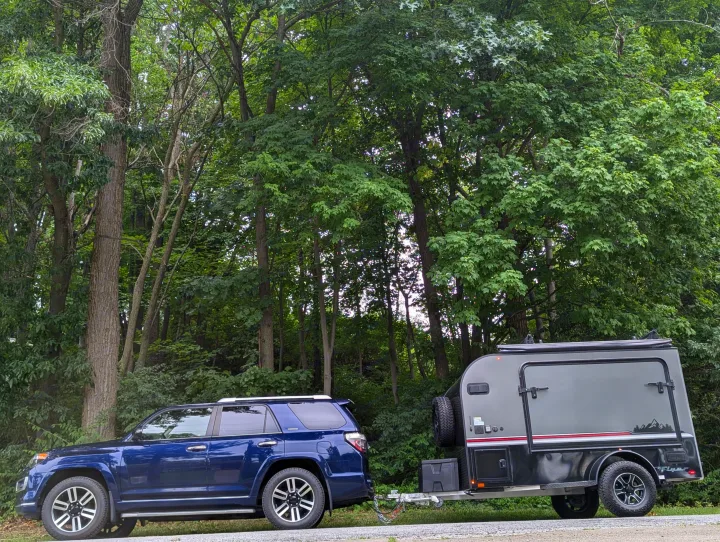 This blue SUV is ready for an rv rental adventure, towing a rugged grey camper trailer surrounded by lush trees.. Intech Flyer Explore 2022