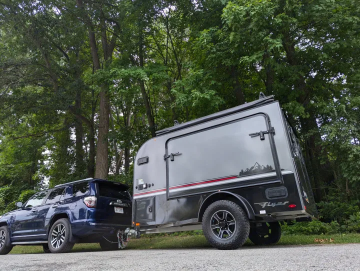 Dark blue SUV towing a gray "Flyer" camper trailer, ideal for an RV rental adventure surrounded by nature.. Intech Flyer Explore 2022