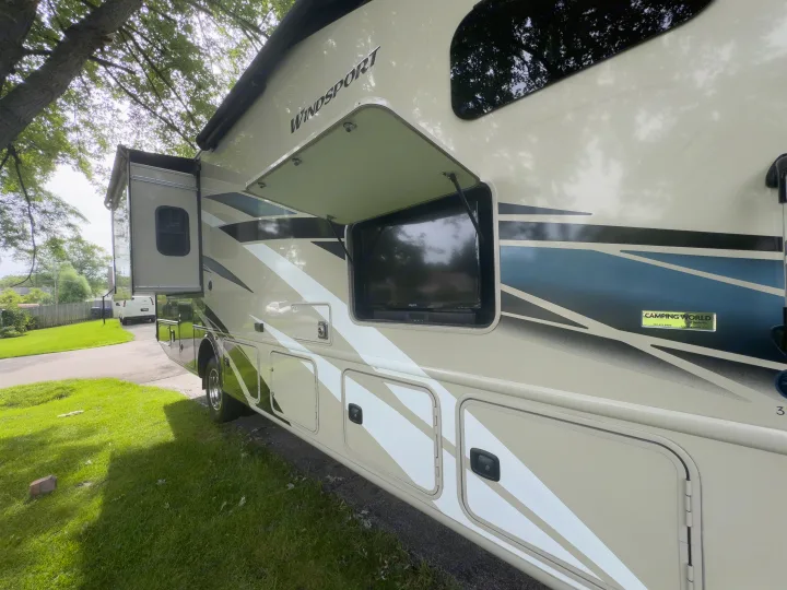A large RV rental motorhome shows its open outdoor TV, ready for camping experiences.. Thor Windsport 2020