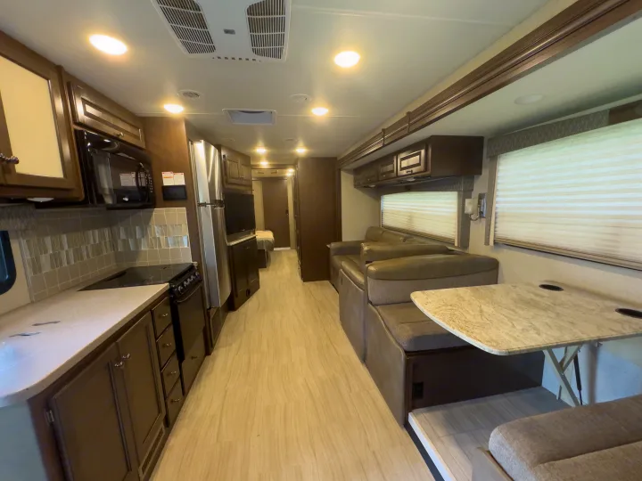 Inside a bright RV rental: modern kitchen, spacious living area with dinette, and light wood floors. Perfect for trips.. Thor Windsport 2020