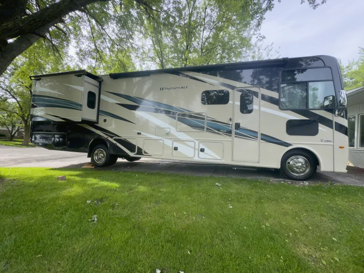 A cream-colored Windsport RV, ideal for an RV rental, is parked on a driveway with its slide-out extended, surrounded by green trees.. Thor Windsport 2020
