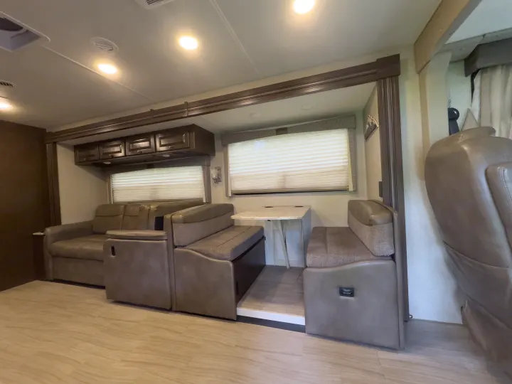 RV rental interior showing a comfortable living space with sofa, dining booth, and overhead cabinets.. Thor Windsport 2020