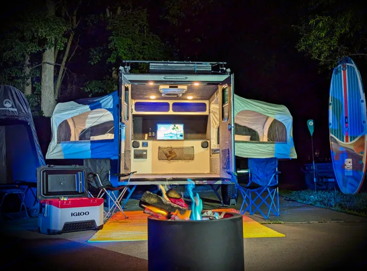 Nighttime RV rental setup: lighted camper, tents, fire pit, cooler, paddleboard for ultimate outdoor living.. Intech Flyer Explore 2022