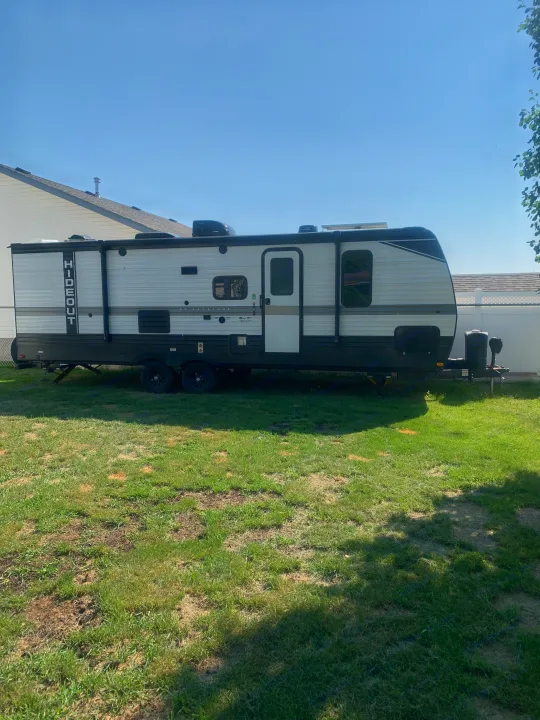 White and grey Hideout travel trailer (RV) available for rv rental, parked on a sunny green lawn.. Keystone RV Hideout 2023
