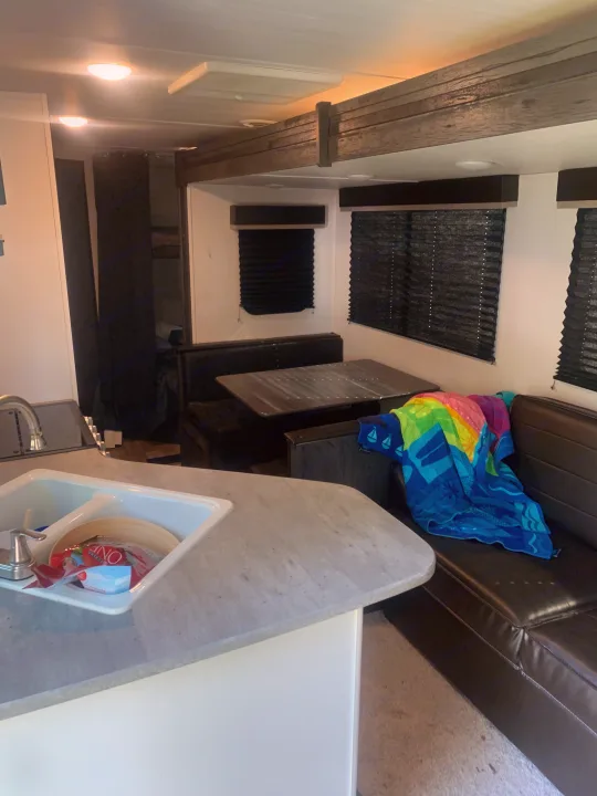 Spacious RV rental interior featuring a bright kitchen sink area, a dinette with bench seating, and a colorful towel on the couch.. Keystone RV Hideout 2023
