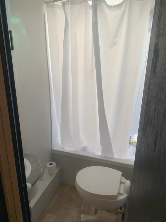 Compact RV rental bathroom features a shower with white curtain, toilet, and accessible toilet paper. Practical space!. Keystone RV Hideout 2023
