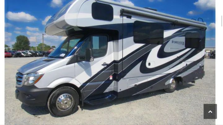 Sleek silver, black & white RV rental motorhome on a gravel lot under blue sky. Note the flat front tire on this Class C camper.. Forest River Mercedes 2019