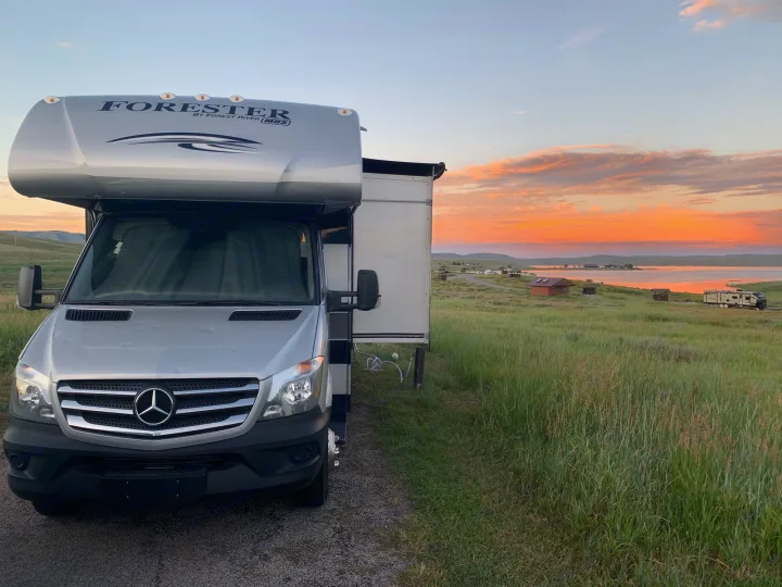 A silver Mercedes-Benz Sprinter RV rental parked by a lake, bathed in the warm glow of a stunning sunset.. Forest River Mercedes 2019