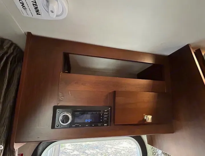 RV rental interior: a dark wood overhead cabinet with an integrated media player and small storage door. KING JACK antenna visible.. Forest River Mercedes 2019