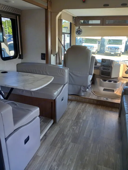 Spacious RV rental interior with a comfortable dinette, front cockpit, and modern wood-look flooring.. Thor Motor Coach Hurricane 2022
