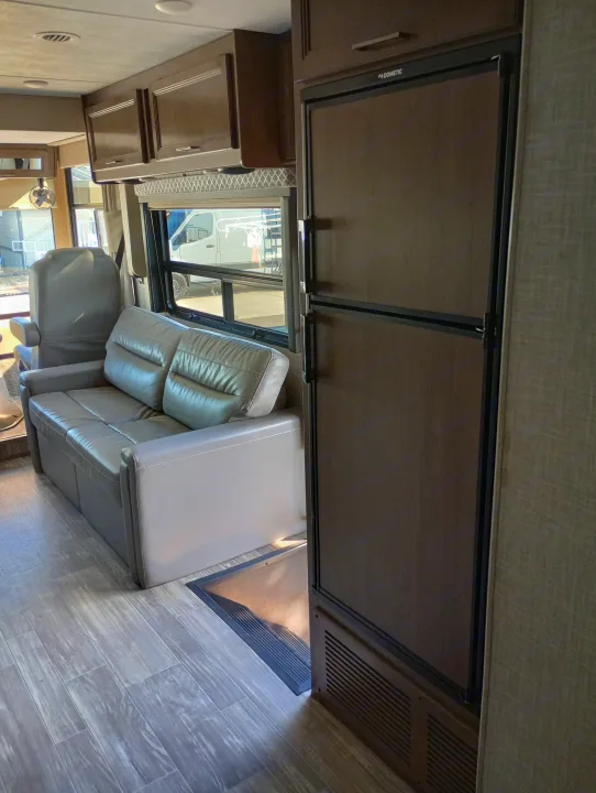Interior of an **rv rental** showing a Dometic refrigerator, leather sofa, wood cabinets, and wood-look flooring.. Thor Motor Coach Hurricane 2022