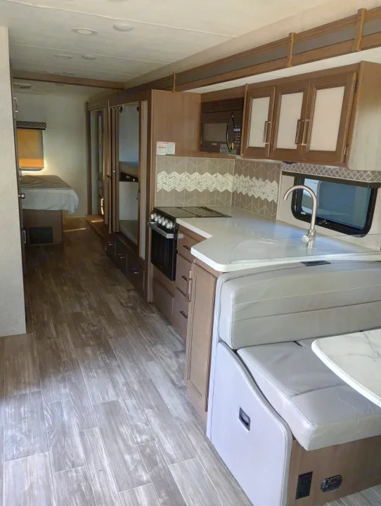 Spacious rv rental interior with a well-equipped kitchen, comfortable dining booth, and private bedroom beyond, ideal for travel.. Thor Motor Coach Hurricane 2022