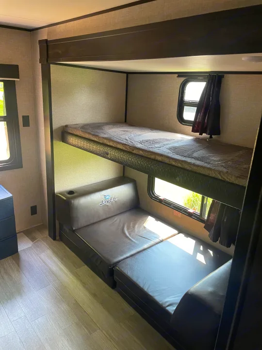 RV rental interior: cozy bunk beds with Jayco logo on convertible lower bed, windows, and light wood flooring.. Jayco Jay Flight 2022