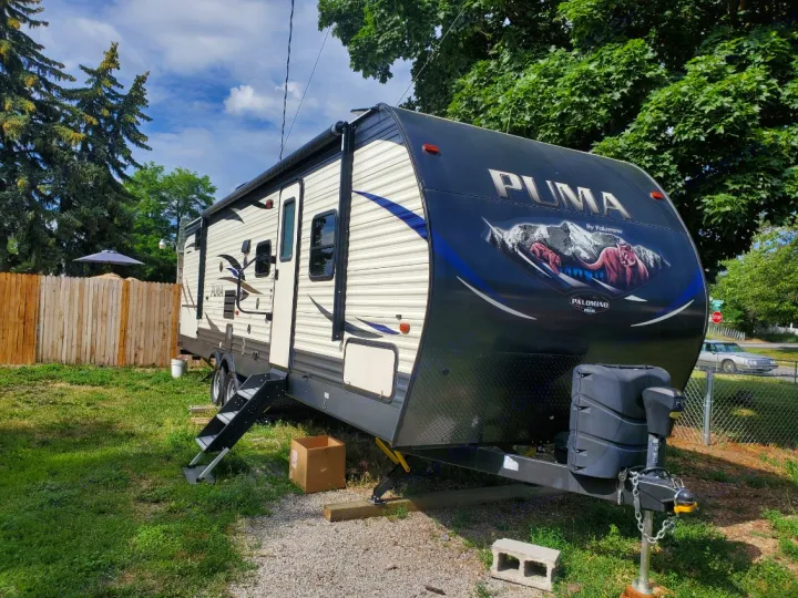 Puma travel trailer RV rental parked outdoors: A large, black and beige unit with extended steps.. Forest River Palomino Puma 2018
