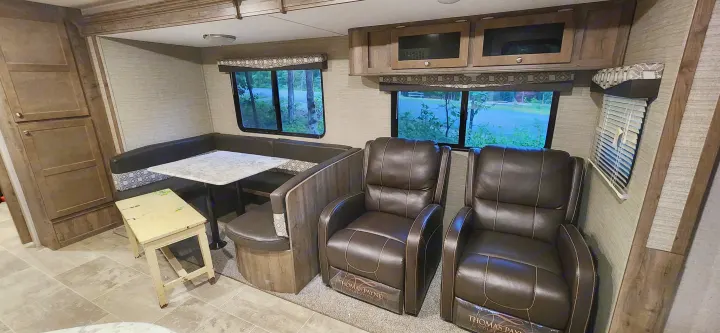 Spacious RV rental interior with a U-shaped dining booth, two leather recliners, and overhead cabinets.. Aspen Trail Aspen Trail Trailer 2019