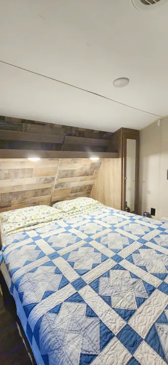 Relax in this RV rental's cozy bedroom. Features a comfortable bed with a blue quilt & wood paneling.. Aspen Trail Aspen Trail Trailer 2019