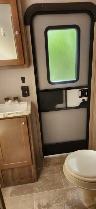 Inside an rv rental: compact bathroom featuring a sink, toilet, and the main entry door, offering a glimpse of nature outside.. Aspen Trail Aspen Trail Trailer 2019