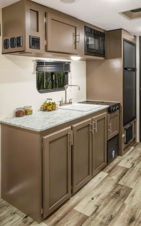 Modern RV rental kitchen with wood-look flooring, gray cabinets, sink, stovetop, microwave, and fridge.. K-Z RV Sportsmen Classic 2024